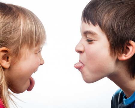 38791925 - close-up shot of boy and girl sticking out tongues to each other on white background. children are half-siblings.